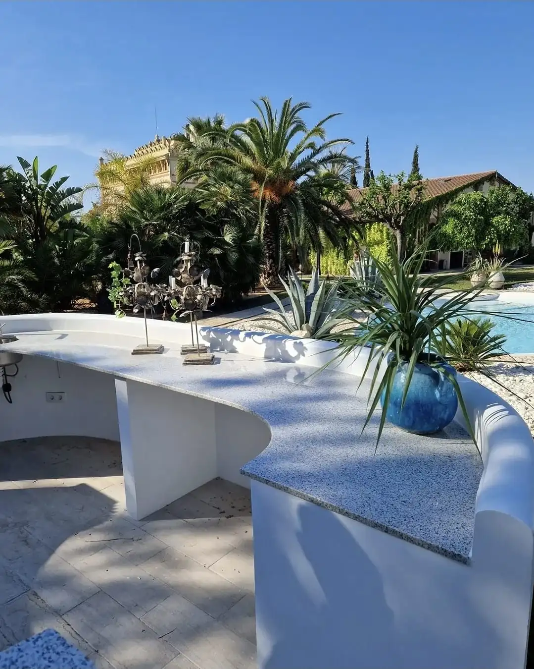 Barra corba d’exterior en granit al costat d’una piscina, amb un edifici modernista al fons