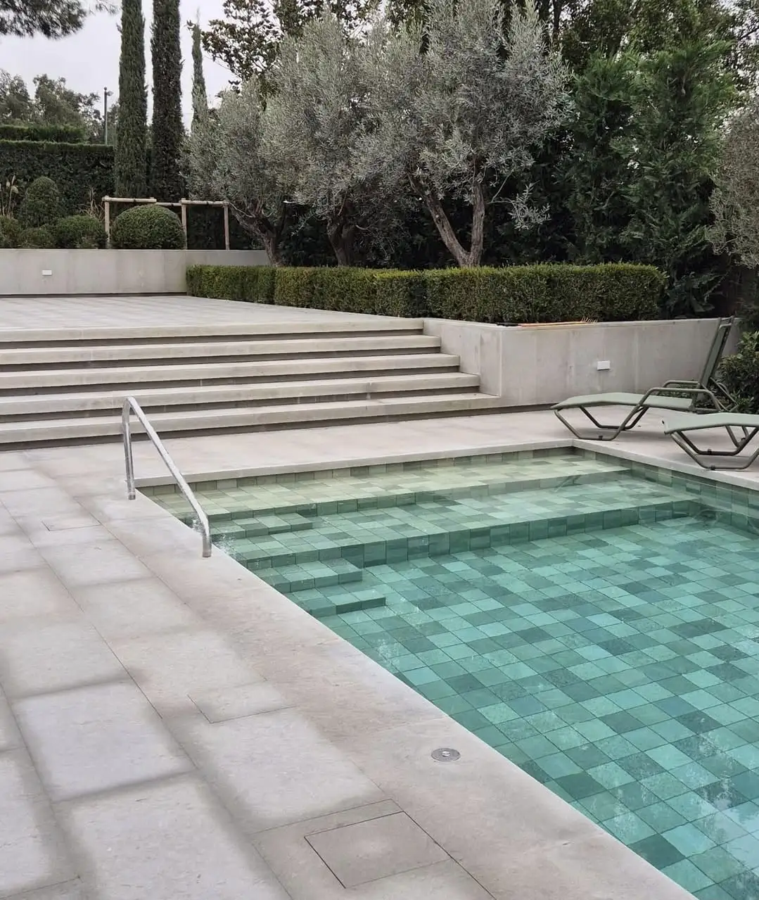 Piscina amb coronament i escalinata de calcària clara entre oliveres i xiprers